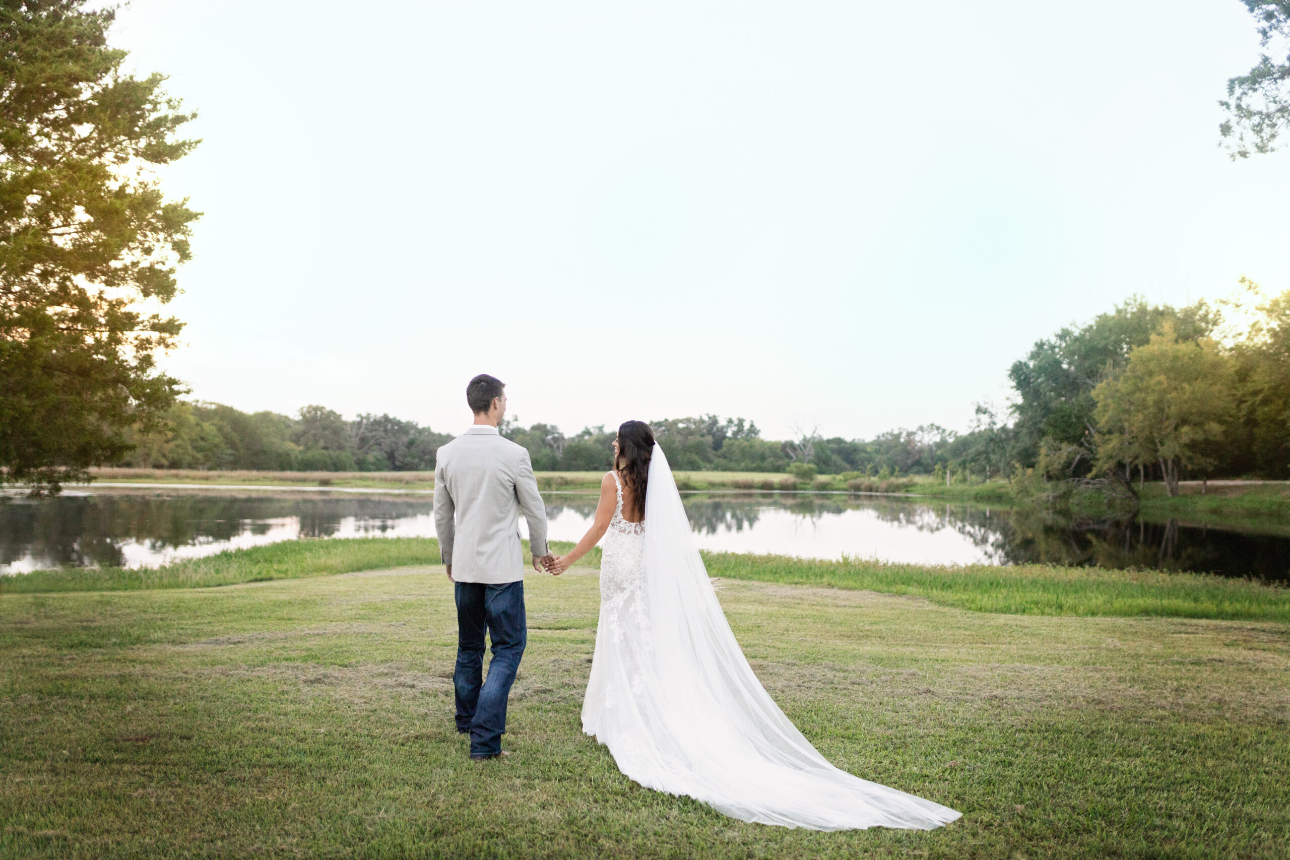 Bride and Groom holding hands and walking away from Dallas Wedding Photographer towards the lake